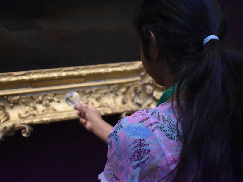A child looks through a lens at a painting.