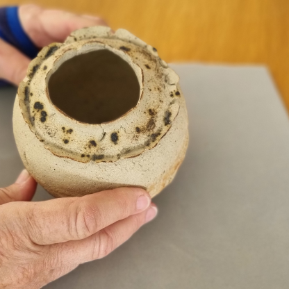 hands of a adult with wrist in a splint holding a round pottery vase on a grey may